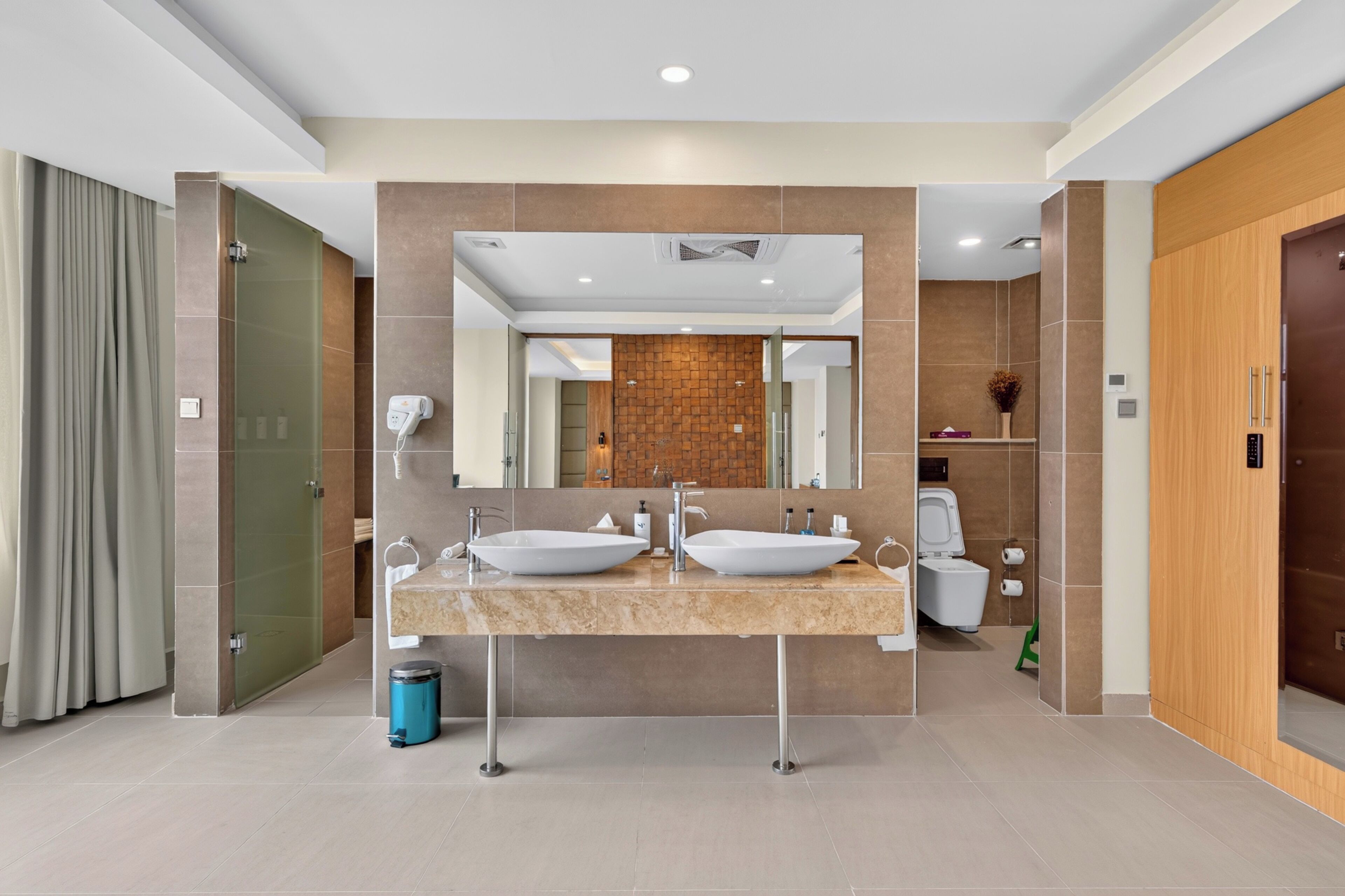 A modern bathroom with two sinks, a mirror, and a toilet.