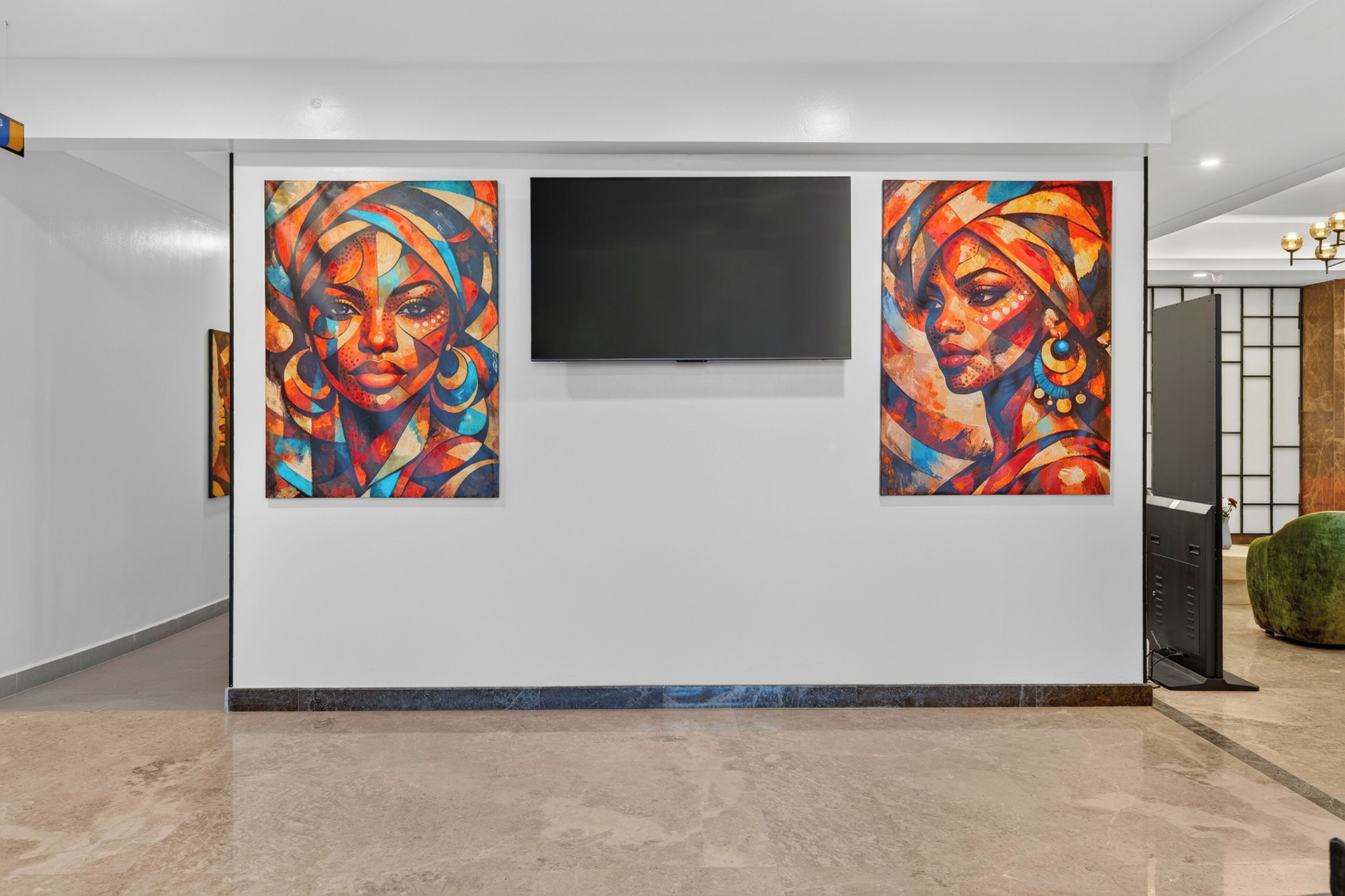 A hallway with two large abstract paintings on the wall, a flat-screen TV mounted above them, and a green upholstered chair in the corner.