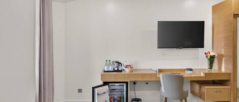 Habitación de hotel con escritorio de madera, televisor de pantalla plana, mini refrigerador, silla y cesto de basura.