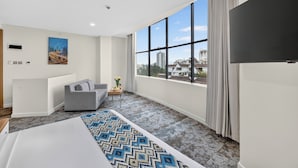 A hotel room with a large window, a bed, a sofa, a small table, and a painting on the wall.