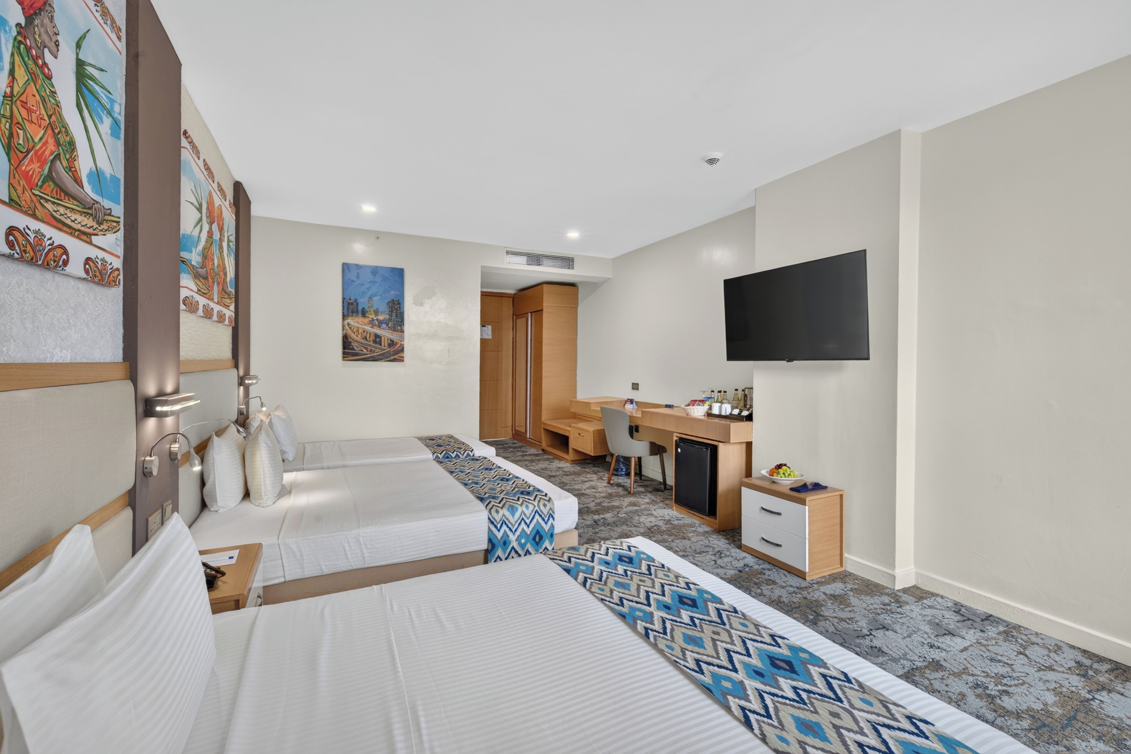 Ein Hotelzimmer mit zwei Betten, einem Schreibtisch, einem Fernseher und Bildern an den Wänden.