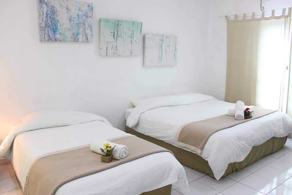 A hotel room with two beds, beige and white bedding, and artwork on the walls.