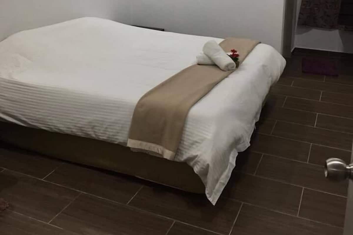 A neatly made bed with a brown throw blanket and a white pillow, a ceiling fan, and an air conditioning unit on the wall.