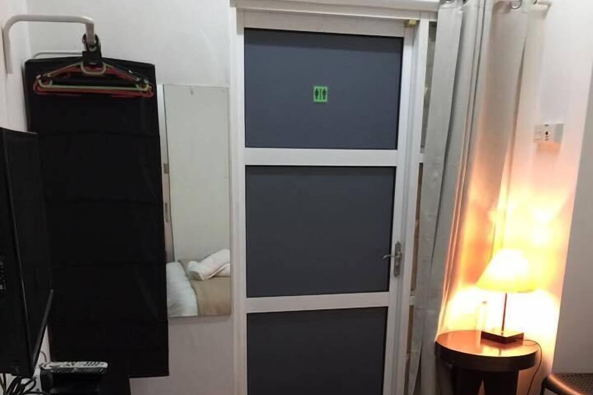 A hotel room with a bed, a desk with a TV, a lamp, and a wardrobe.