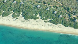 Ett flygbildsbild av ett semesterområde vid stranden med flera bungalovliknande byggnader, omgivet av tät vegetation.