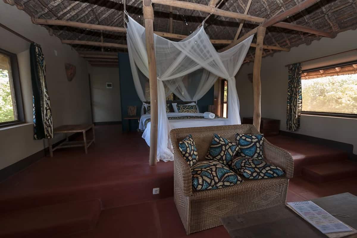 A room with a bed, a wicker sofa, a hanging canopy, and a window with a view.
