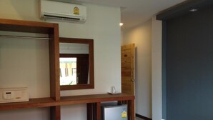 A hotel room with a bed, a small refrigerator, a microwave, an air conditioner, and a wooden shelf with a mirror. - Rin Bay View Resort (Ko Pha-ngan)