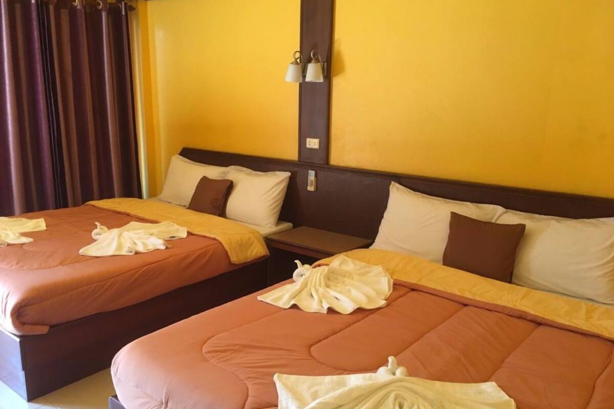 Two double beds with matching brown headboards and white pillows, a nightstand between them, and a wall-mounted light fixture.