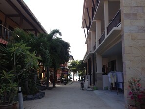 A narrow street with buildings on either side, featuring balconies and potted plants.