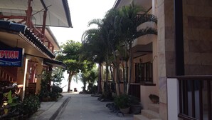 A narrow street with buildings on either side, lined with palm trees and potted plants. - Rin Bay View Resort (Ko Pha-ngan)