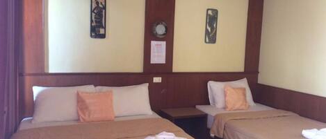 Habitación de hotel con dos camas, cada una con una almohada y una toalla doblada. Hay relojes en la pared y un cuadro enmarcado.