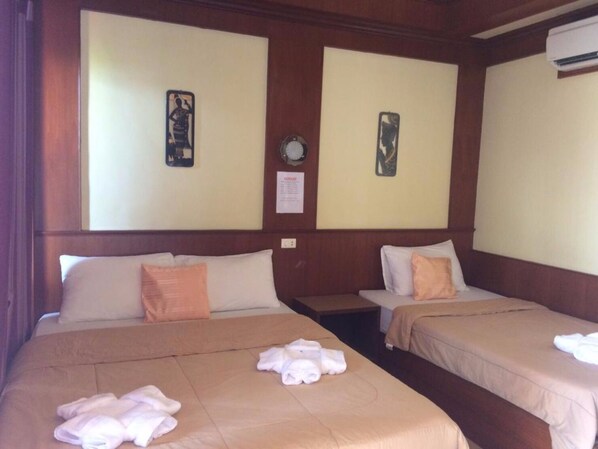 A hotel room with two beds, each with a pillow and a folded towel. There are wall-mounted clocks and a framed picture on the wall.