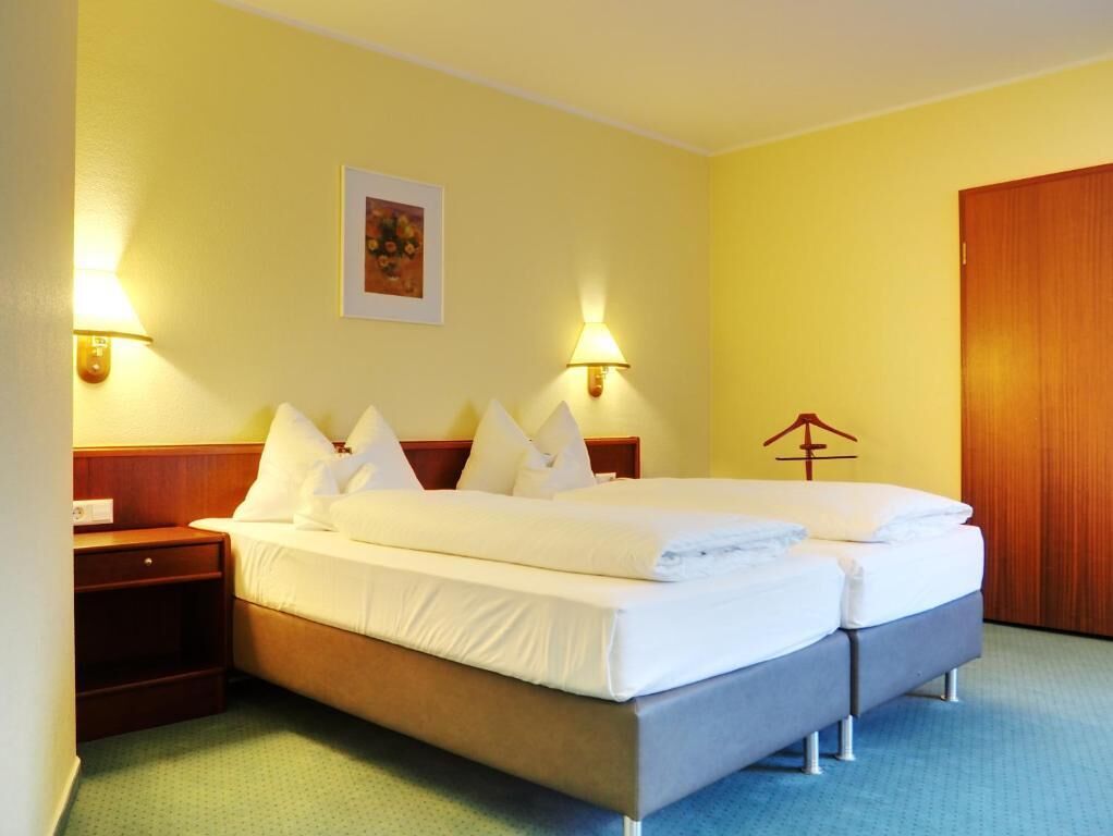 Habitación de hotel con cama doble, dos mesitas de noche, un armario de madera y un cuadro enmarcado.