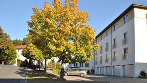 A multi-story building with a parked car in front, a tree with autumn leaves, and a clear sky. - Heidehotel Lubast (Kemberg)
