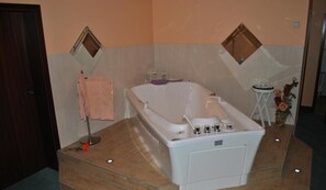 A bathroom with a large bathtub, a small round table with a vase of flowers, and a mirror on the wall. - Heidehotel Lubast (Kemberg)