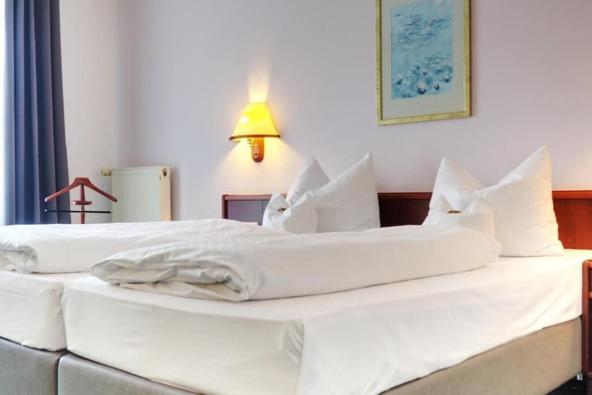 A hotel room with a bed, a nightstand, a lamp, and a painting on the wall.
