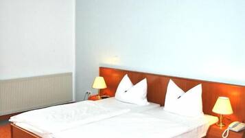 A hotel room with a large bed, two bedside tables with lamps, and a radiator under the bed.