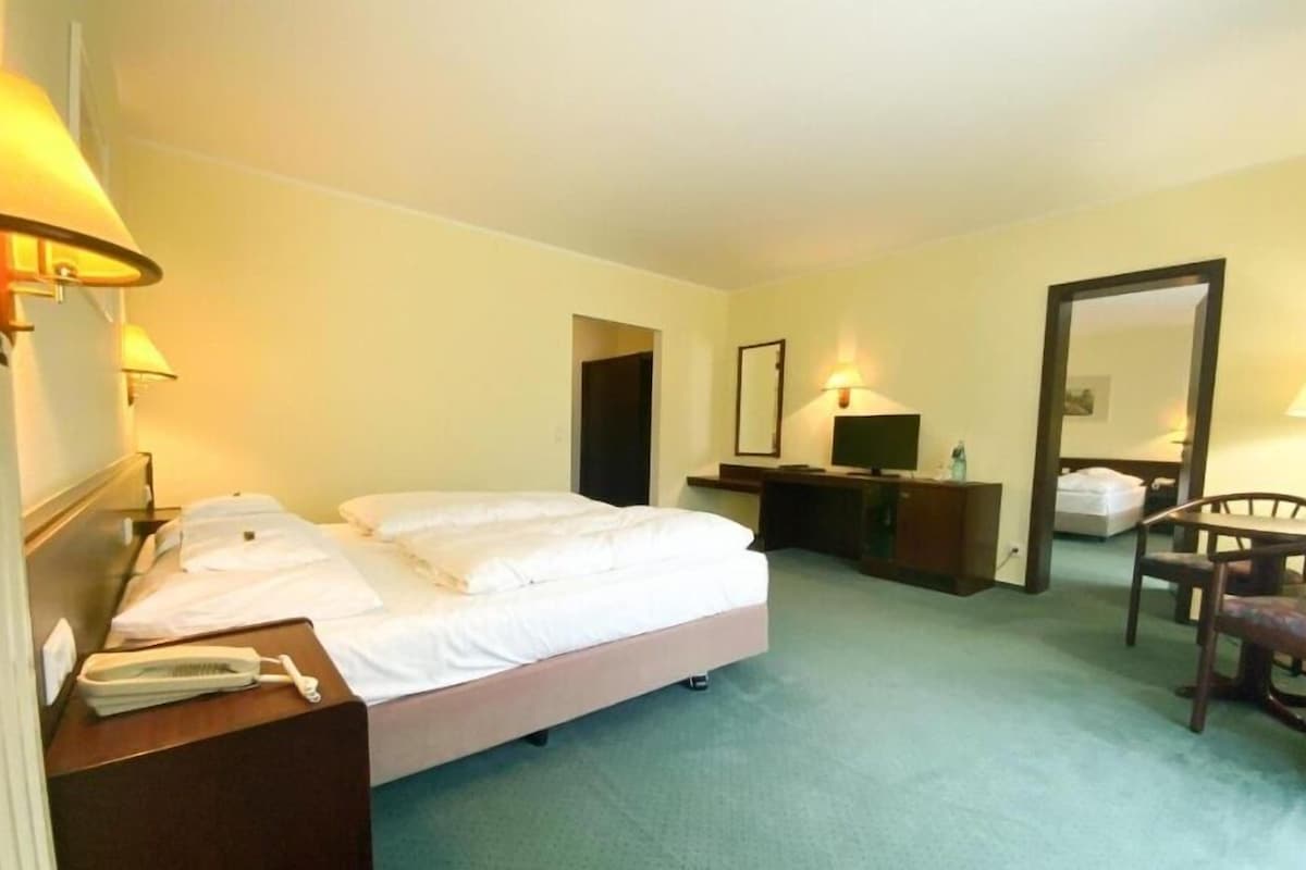 A hotel room with a bed, bedside table, lamp, dresser, mirror, and a chair.