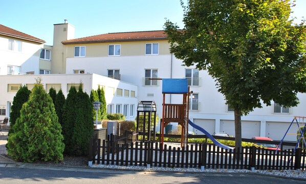 Um edifício residencial com parquinho, cerca e uma árvore.