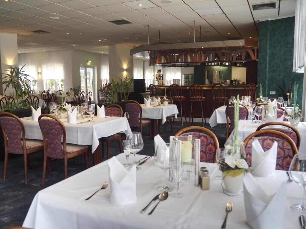 Ein Restaurant mit mehreren gedeckten Tischen, ausgestattet mit weißen Tischdecken, Stühlen und Gläsern.