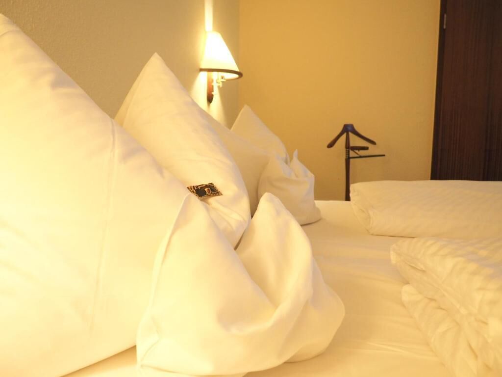 Quarto de hotel com cama bem arrumada, luminária fixada na parede e placa simples na parede.