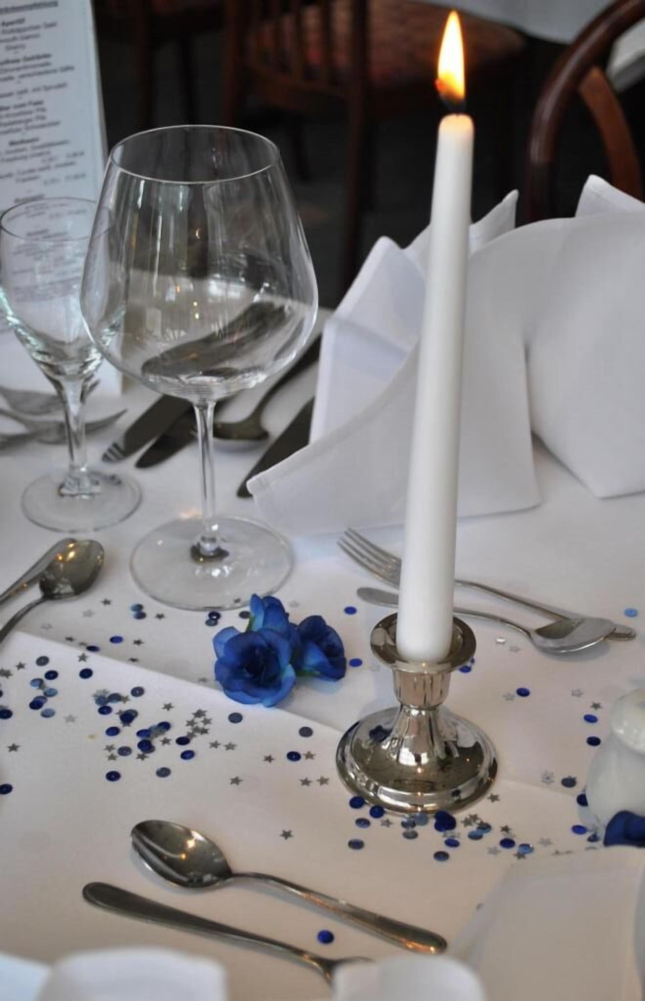 Een gedekte tafel met een witte tafelkleed, bestek en een brandende kaars.