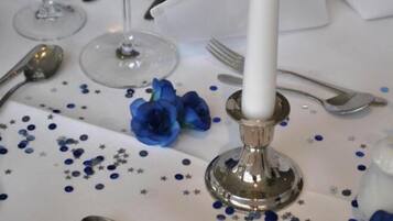 Een gedekte tafel met een witte tafelkleed, bestek en een brandende kaars.