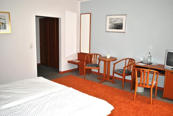 Habitación de hotel con una cama, un escritorio con silla, un televisor y un cuadro en la pared.