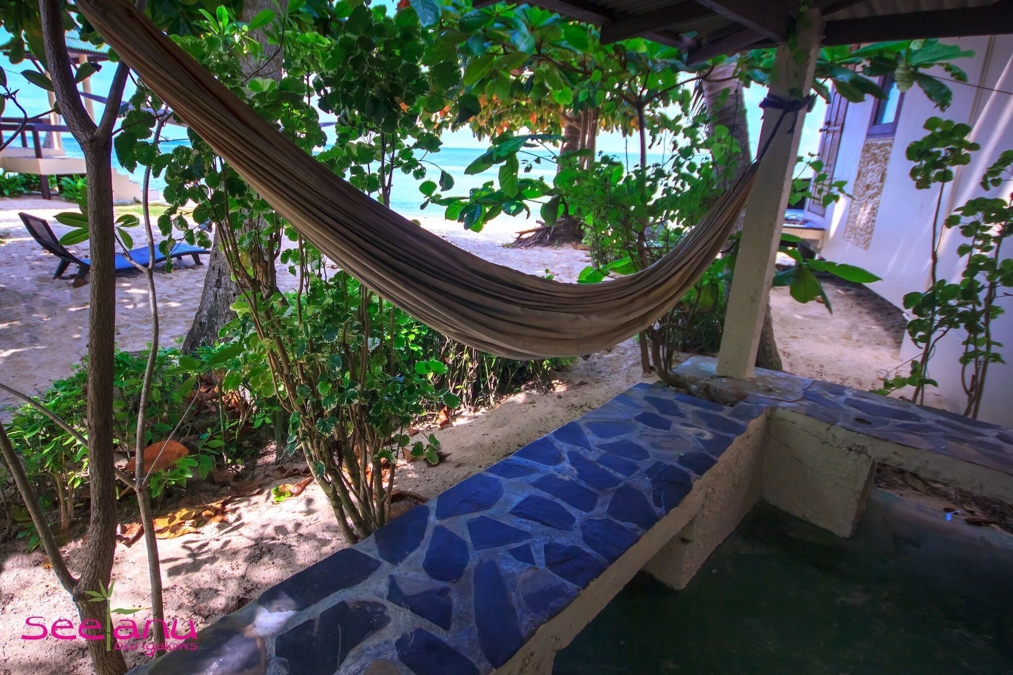 Un hamac installé dans un espace ombragé, avec vue sur la plage et des chaises longues à proximité.