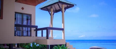 A beachfront property with a covered seating area, a view of the ocean, and a palm tree.