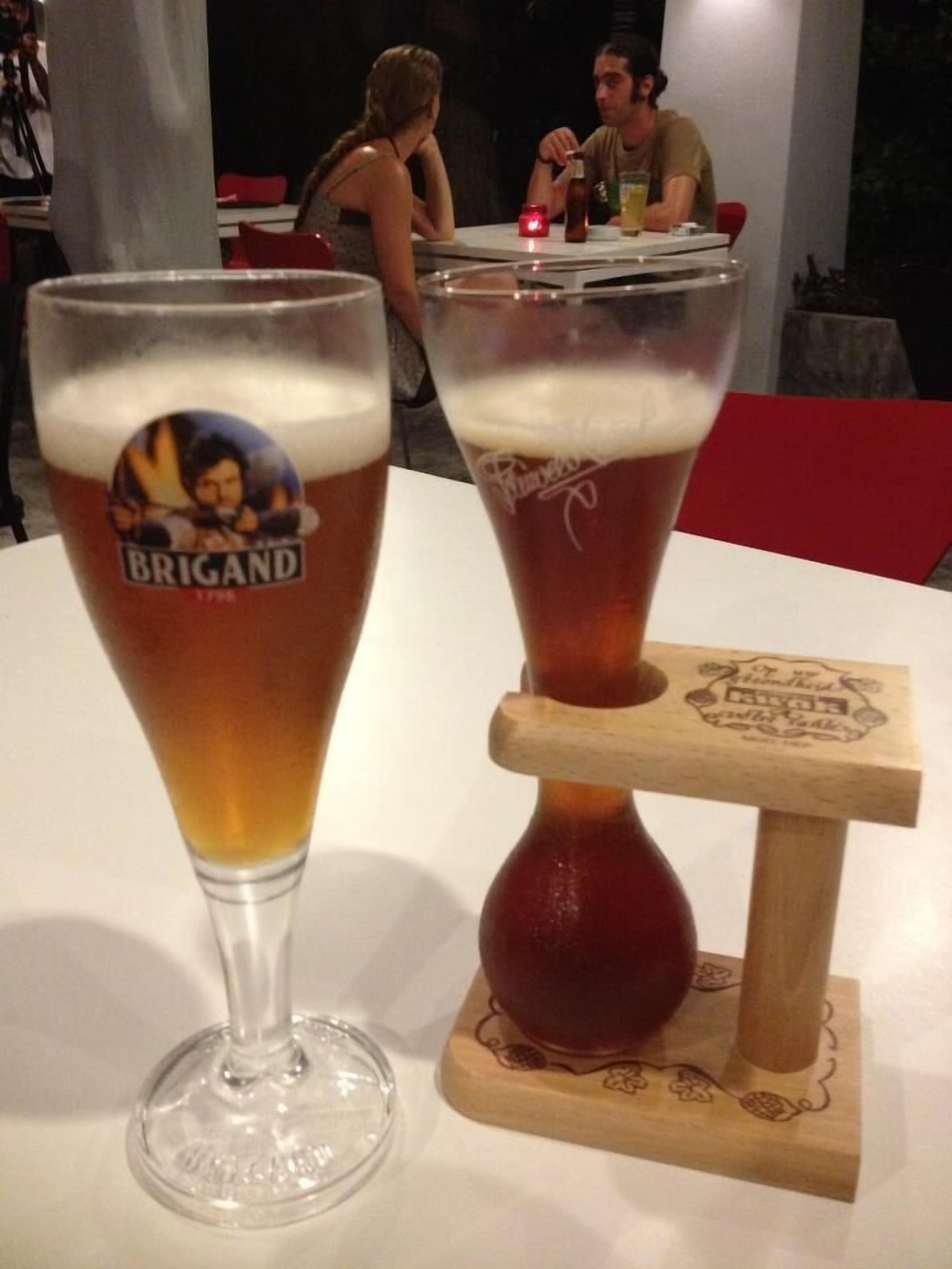 Two glasses of beer on a table, one with a label reading "Brigand" and the other with a wooden coaster.