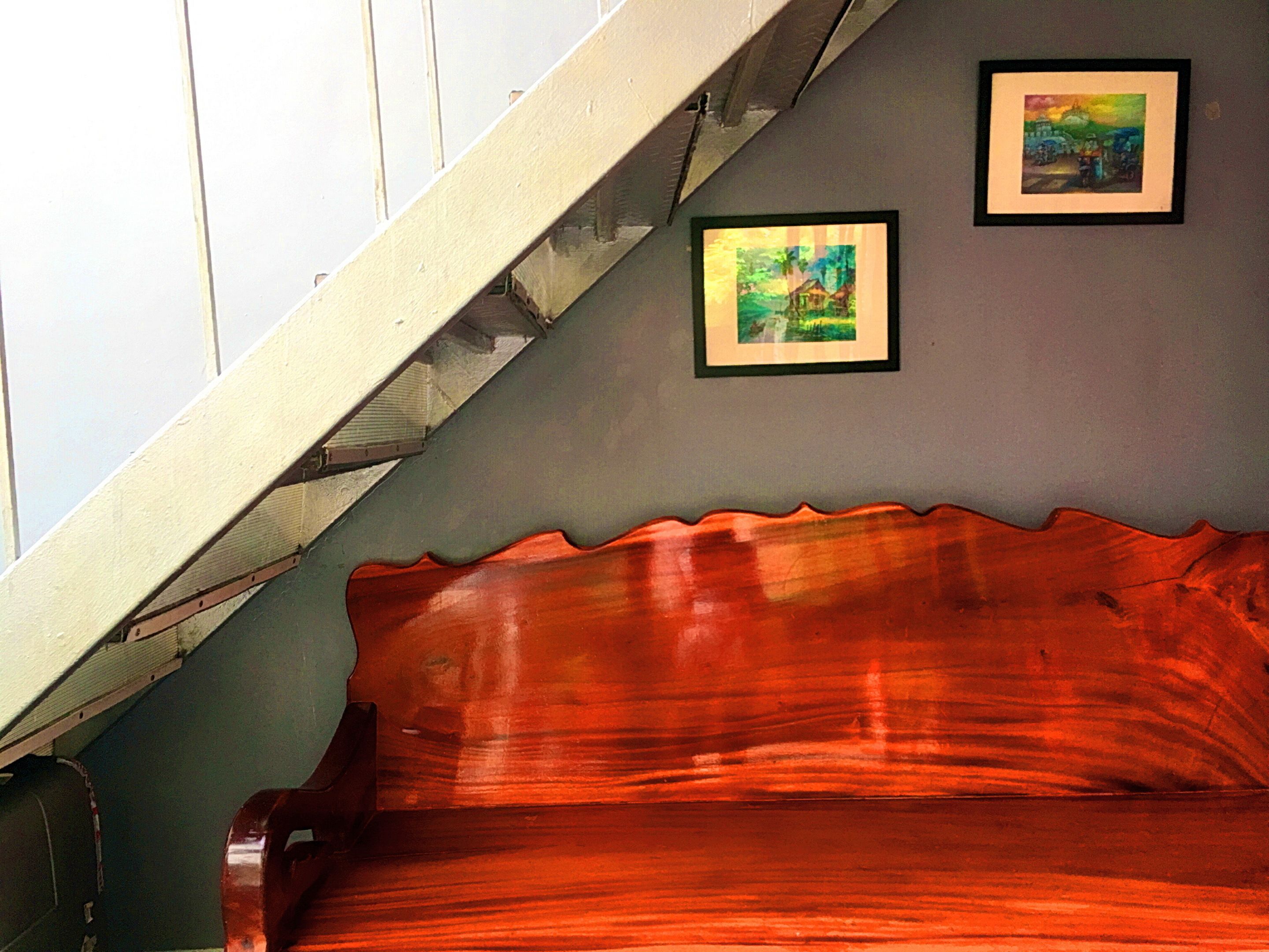 Una escalera con barandilla de madera y un banco tapizado de rojo.