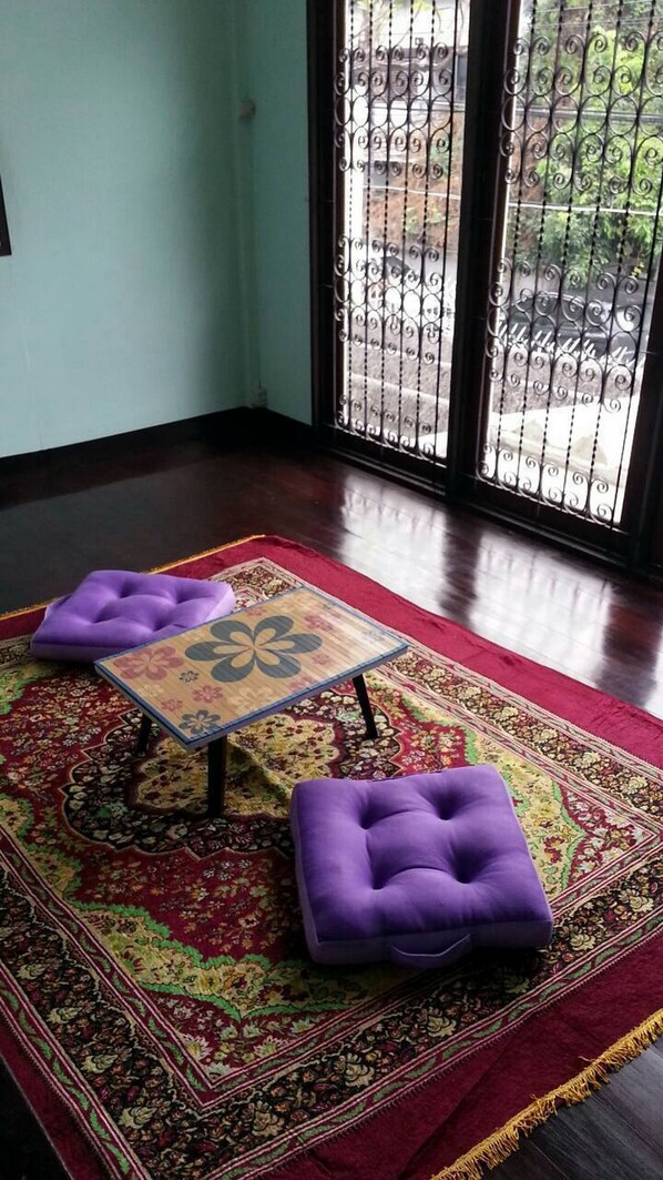 Une pièce avec un tapis à motifs, deux poufs violets et une petite table ornée de motifs floraux.