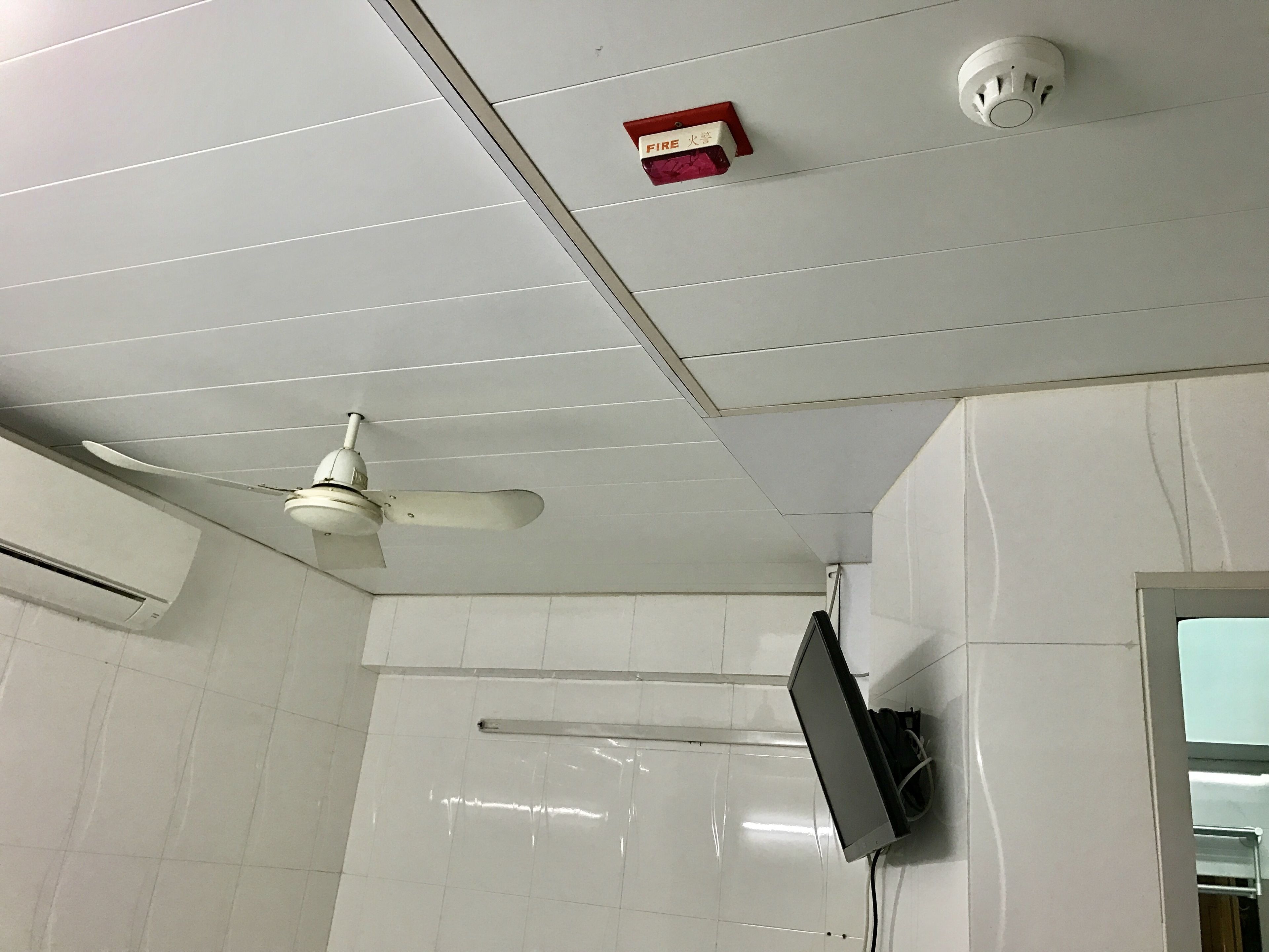 A ceiling with a ceiling fan, a smoke detector, and a fire alarm.
