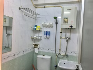 A bathroom with a toilet, sink, shower, and storage shelves. - Beverly Guest House (Kowloon)