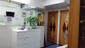 A bathroom with a white sink, a mirror, a potted plant, and wooden doors. - Beverly Guest House (Kowloon)