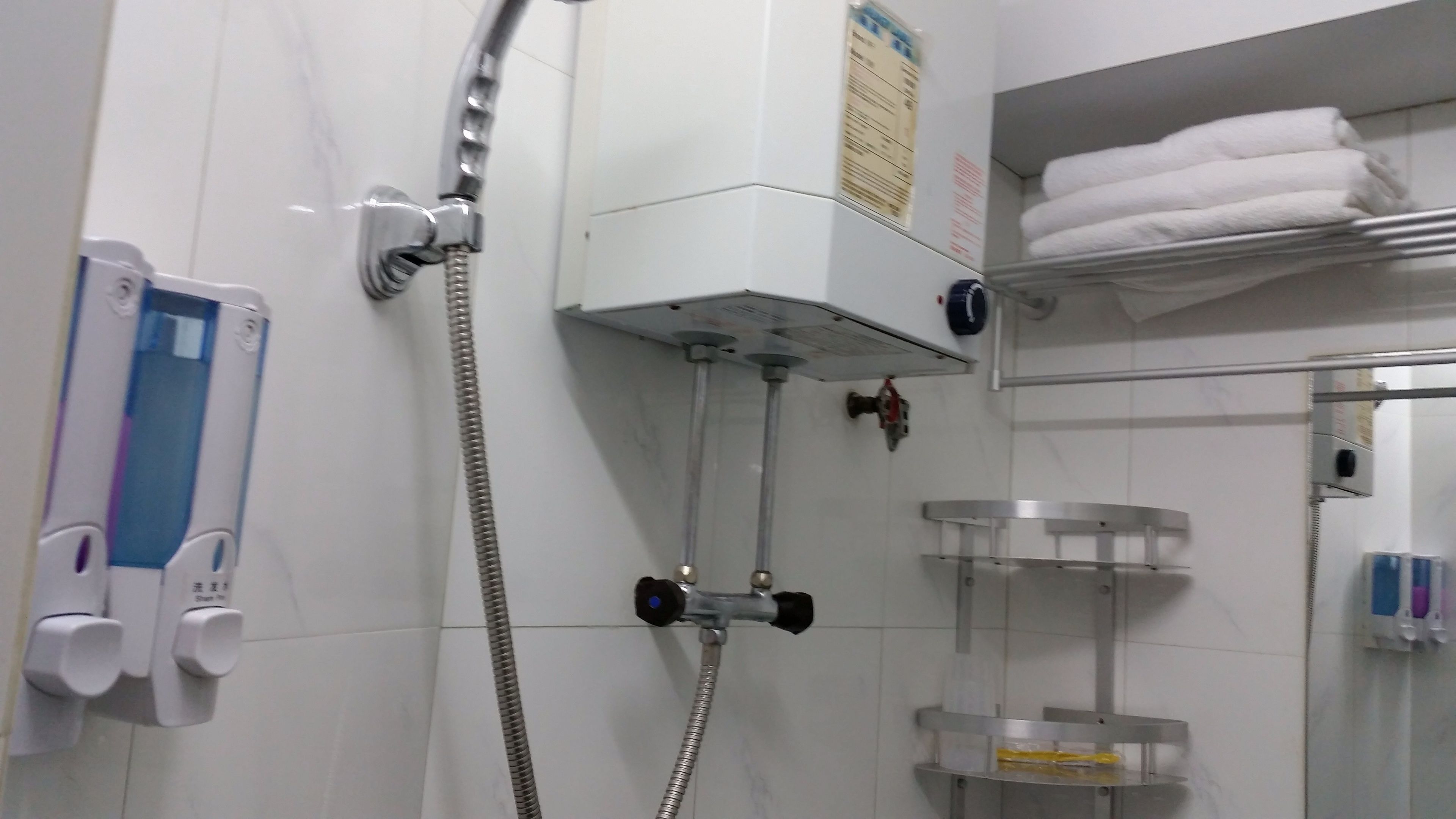 A bathroom with a shower, a towel rack, and a soap dispenser.