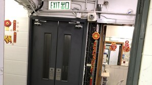 A hallway with an exit sign, a door with push buttons, and a tiled floor. - Beverly Guest House (Kowloon)