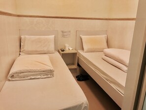A small, clean room with two single beds, a nightstand with a remote control, and a pair of slippers on the floor. - Beverly Guest House (Kowloon)