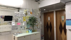 A reception area with a counter, a potted plant, and a wall covered with various papers and notes. - Beverly Guest House (Kowloon)