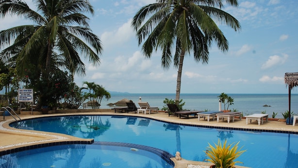 Piscina com espreguiçadeiras e palmeiras, com vista para um corpo de água.
