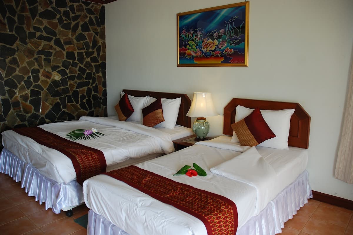 Two single beds with white linens and red decorative borders, a stone wall, a painting of marine life, and a nightstand with a lamp.