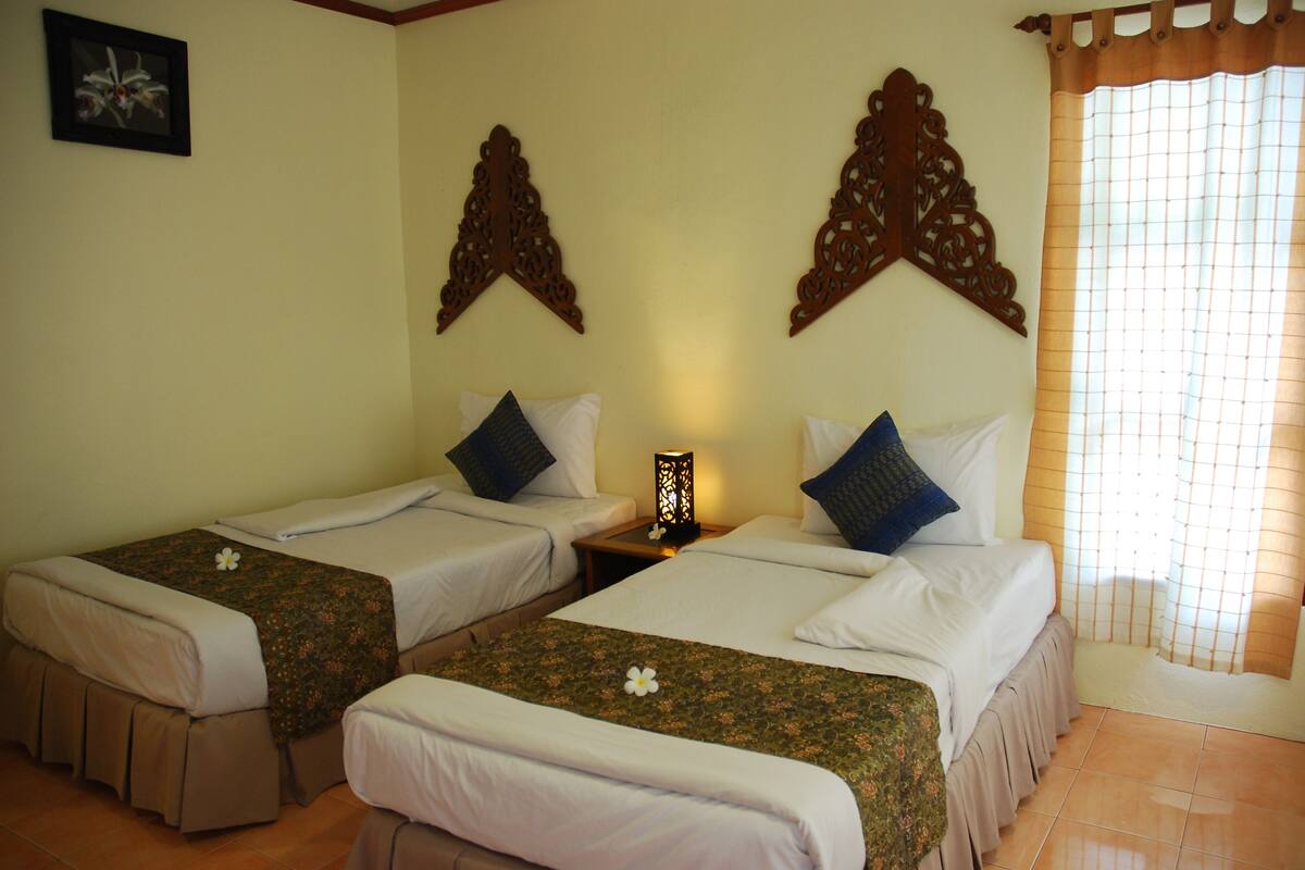 A hotel room with two single beds, a nightstand with a lamp, and a window with a curtain.