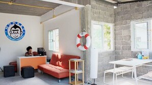 A room with a desk, a sofa, a small table, and a life preserver on the wall. - Monkey Samui Hostel (Koh Samui)