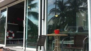 A glass door entrance with a view of palm trees and a red bucket on a table outside. - Monkey Samui Hostel (Koh Samui)