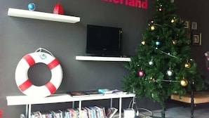 A room with a television on a stand, a Christmas tree, a life preserver decoration, and a shelf with books. - Monkey Samui Hostel (Koh Samui)