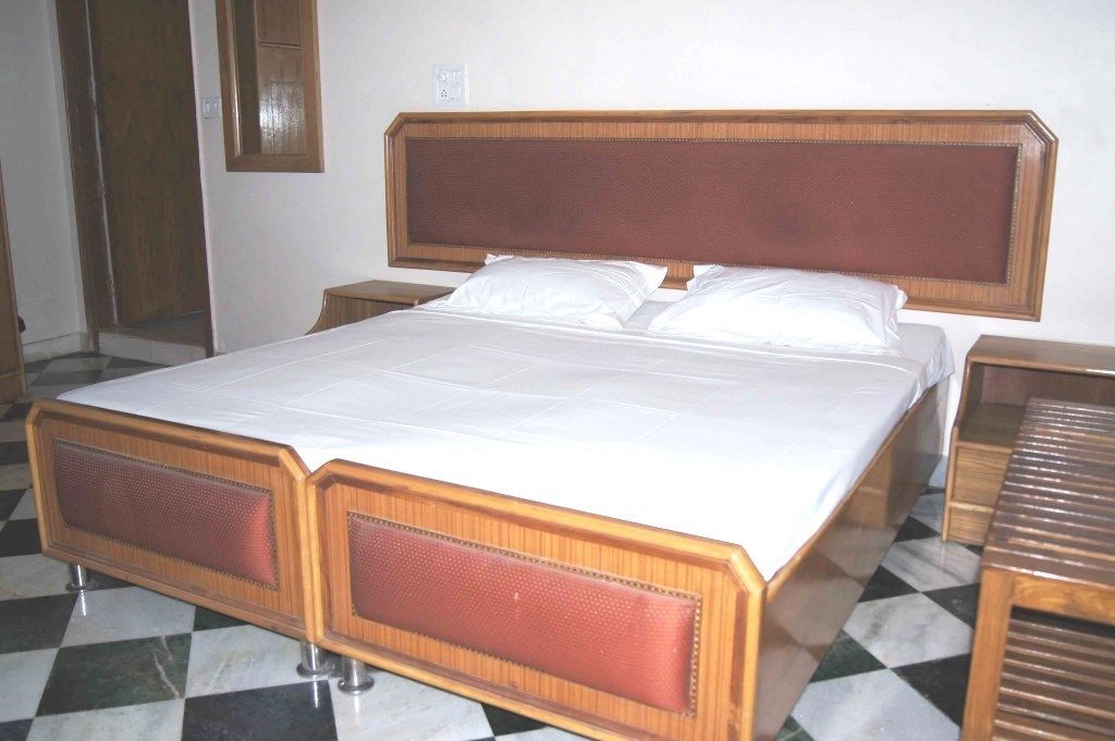 Una habitación de hotel estándar con una cama grande, cabecera de madera y suelo a cuadros.