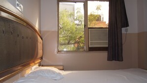 A hotel room with a bed, a window with curtains, and an air conditioning unit. - Westend Holiday Home (New Delhi)