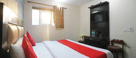 A hotel room with a bed, a desk, a chair, a window with curtains, and a television.