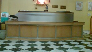 A reception area with a checkered floor, a counter with a light above it, and a wall with a sign and pictures. - Westend Holiday Home (New Delhi)